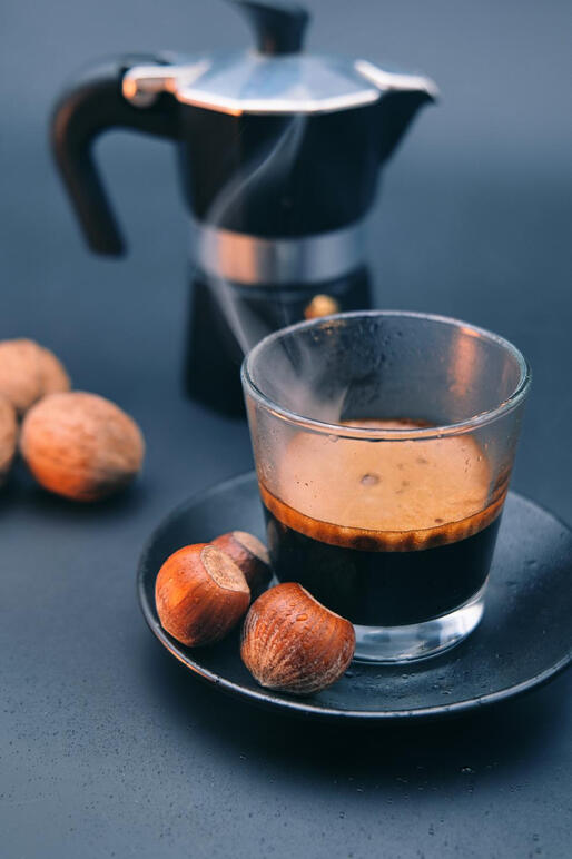 Hot steaming coffee cup with mixed nuts on dark background.